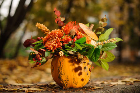 Orange pumpkin with a beautiful autumn flower composition on the background of yellow fallen leavesの写真素材