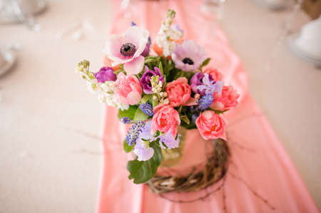 Table decoration made of little vase with beautiful and colorful flowers mixed in stylish bouquet on the pink tableclothの写真素材