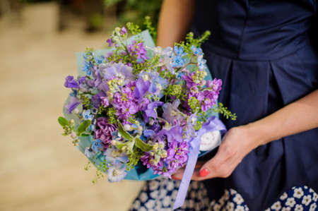 Woman in blue dress is holding a little and beautiful blue and purple flower compositionの写真素材