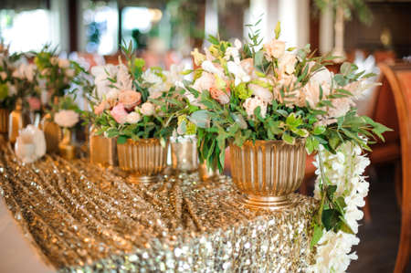 Golden pots with tender and beautiful white roses standing on the golden tablecloth with glittering sequinsの写真素材