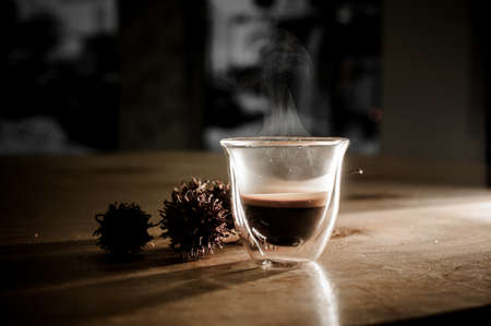 Glass cup of hot coffee with steam from it near dried flowers located on the wooden tableの写真素材