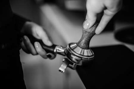 Black and white photo of female barista using a temper to make a coffee tabletの写真素材