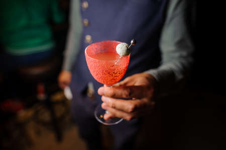Barman holding in hand a decorated glass of alcoholic cocktail on the dark and blurred backgroundの写真素材