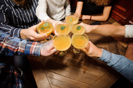 Group of people sitting at the table and clinking glasses of the fresh orange lemonade