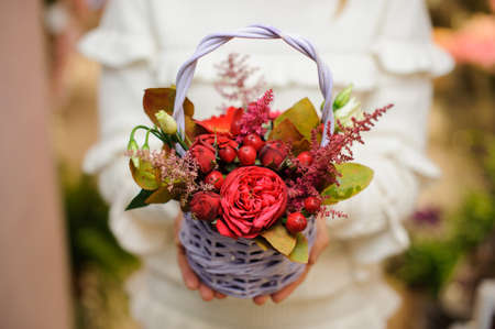 Little pretty wicker basket with flower composition in red tones in woman hands on the light backgroundの写真素材