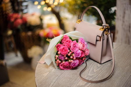 Beautiful pink flower composition near the stylish handbag on the table against the bright backgroundの写真素材