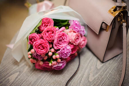 Tender pink flower composition near the stylish and elegant woman handbag on the wooden tableの写真素材