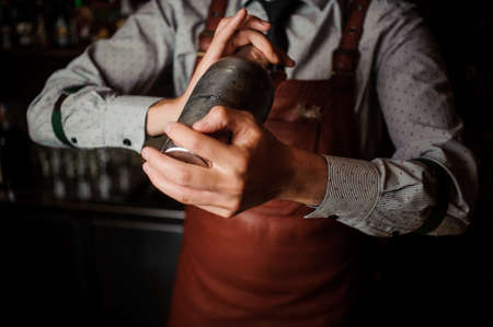 Barman in a brown apron shaking the shaker on the dark background of bar counterの写真素材