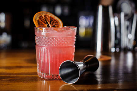 Glass of pink alcoholic cocktail decorated with a slice of orange on the table against the indoors background of a barの写真素材