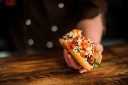 Man sitting at the wooden table holding a tasty hot dog with a grilled sausageの写真素材