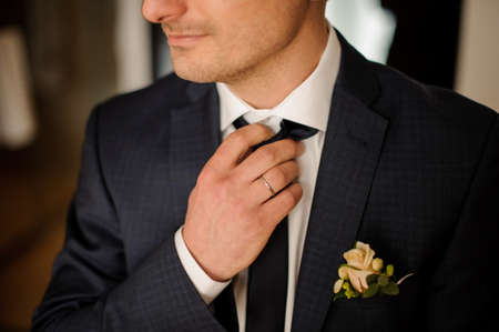 Grooms morning preparation. Handsome groom getting dressed in wedding suit with boutonniere and preparing for the ceremonyの写真素材