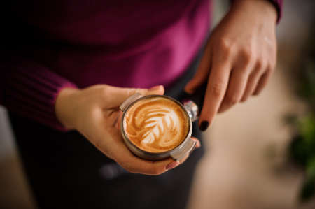 Woman in a purple shirt holding a temper with a beautiful latte art. Coffee conceptの写真素材