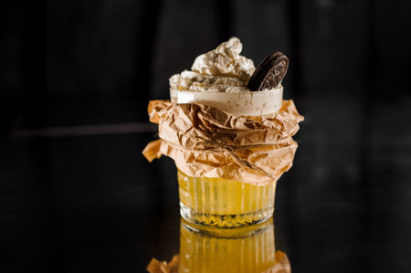 Fresh sweet cocktail with whipped cream decorated with chocolate cookie and wrapped in paper. Drink...