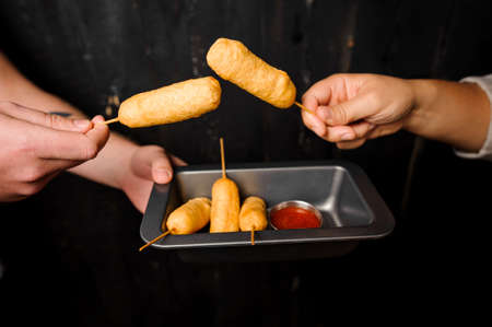 Mans hands holding a plate of cheese sticks with tomato sauce on the dark background. Food conceptの写真素材