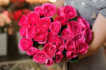 Woman in a grey dress holding a large bright pink flower composition on the indoors background. Bouquet conceptの写真素材