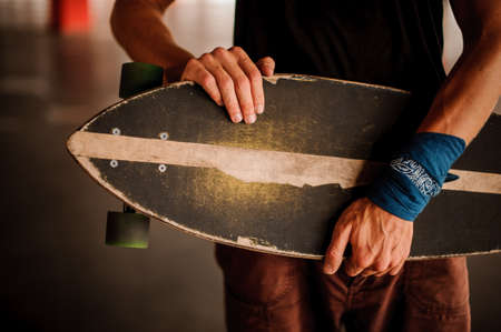 Young man dressed in black T-shirt and with an armband holding a longboard on the grey backgroundの写真素材