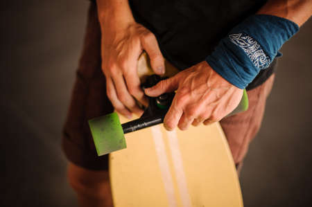 Young mans hands with an armband holding a yellow longboard with green wheels on the grey backgroundの写真素材