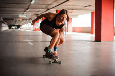 Handsome redhead guy with tattoo riding on a longboard on the floor of a parkingの写真素材