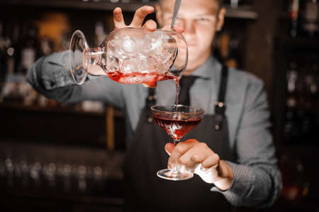 Barman pouring a red alcoholic cocktail into the glass o the background of bar counterの写真素材