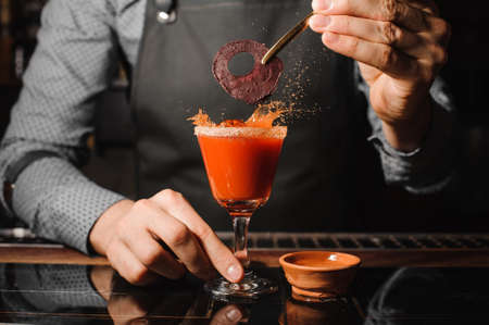 Barman in the grey apron decorating a glass of red alcoholic cocktail on the bar counterの写真素材