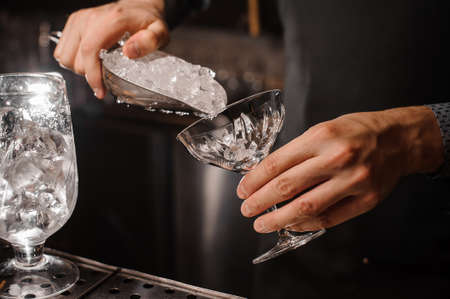 Bartender hand putting ice into the cocktail glass on the grey background on bar counterの写真素材