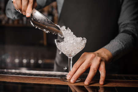 Barman putting ice into the cocktail glass against the blurred background of the bar counterの写真素材