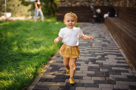 Sweet little girl in cute clothing walking and smiling outdoors near the fresh green grassの写真素材