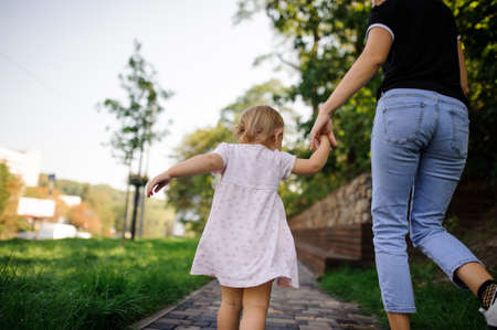 Back view of cute little girl dressed in a pretty pink dress walking with motherの写真素材