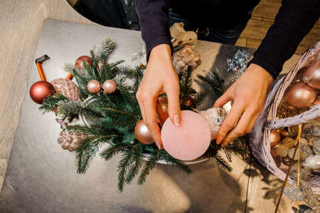 Florist making a beautiful Christmas decoration composition with pretty candles, glass balls and fir treeの写真素材