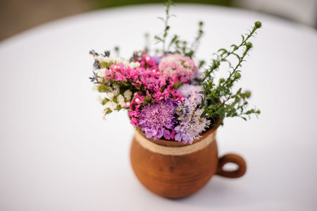 Cute clay pot with a pretty bouquet of colorful flowers on the background of white table