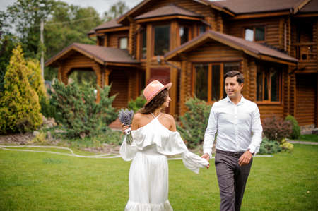 Happy and beautiful married couple on the background of big wooden house and green grassの写真素材