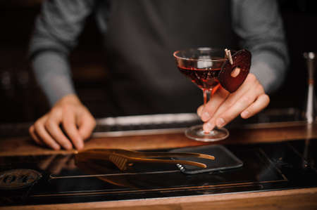 Barman hand holding a glass of red alcoholic drink, decorating with a thin slice of beetの写真素材