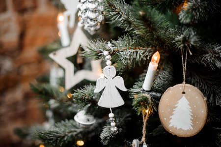 Christmas tree branches decorated with snow, garlands and cute wooden toys in white tones hanging on itの写真素材