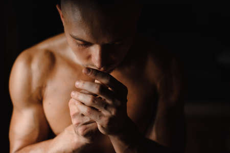 Close up portrait of the muscular and tanned athletic guy with closed eyes and holding hands near the faceの写真素材