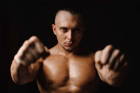 Muscular, sexy and tanned guy with bristles clenching his fists on the black background of studioの写真素材