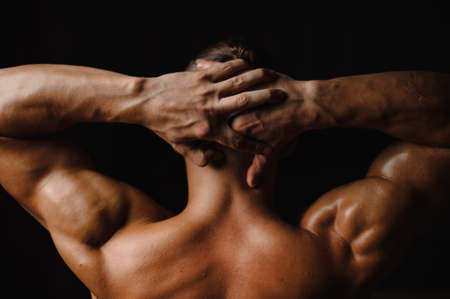 Back view of the sexy muscular bodybuilder s back and hands on the black background of studioの写真素材