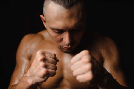 Strong amd muscular man clenching his fists with closed eyes on the black background of studioの写真素材