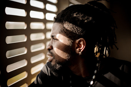 Attractive afro-american man with dreadlocks and dressed in black clothes looking out of the window