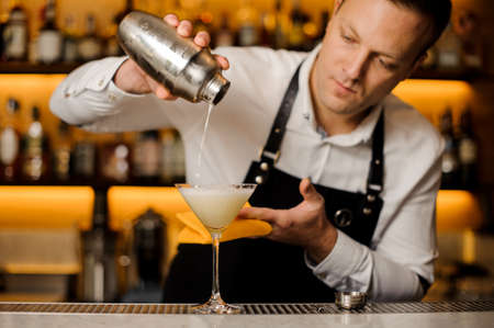 Barman pouring a fresh alcoholic drink into an elegant cocktail glass on the bar counterの写真素材