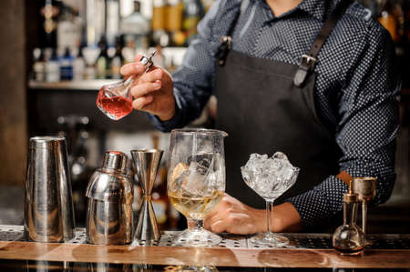 Barman pouring fruit syrup into the large cocktail glass with ice cubes on the bar counterの写真素材