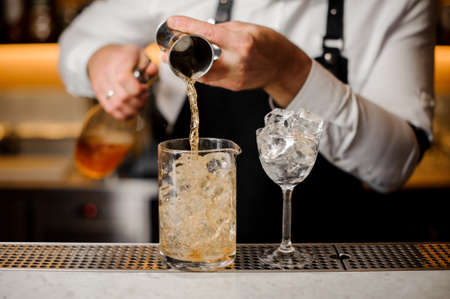 Barman pouring a portion of alcoholic drink into a glass filled with ice cubes on the bar counterの写真素材