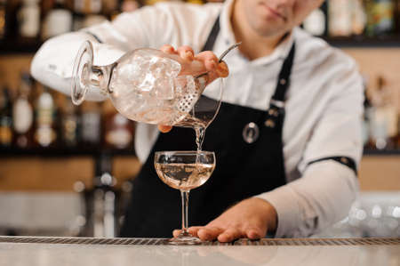 Bartender adding vodka mixed with ice cubes into a cocktail glass on the bar counterの写真素材