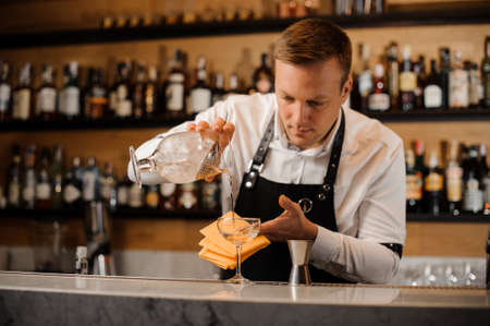 Barman pouring alcoholic drink mixed with ice into a cocktail glass on the bar counterの写真素材