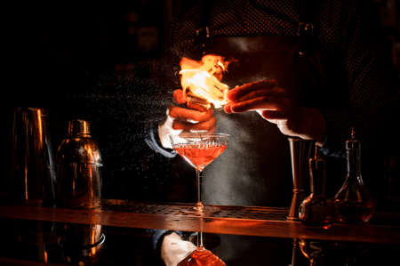 Barman making a fresh alcoholic cocktail with a smoky note on the dark bar counterの写真素材