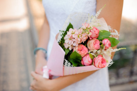 shapely woman in white dress holds a bouquet of pion-shaped roses, astilba and roses packed in white and pink wrapping-paperの写真素材