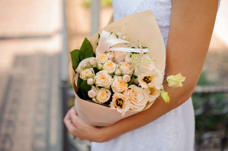 shapely female in white dress holds a bouquet of eustoma , astilba and roses packed in apricot wrapping-paper and pink ribbonの写真素材