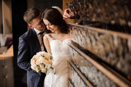 pretty bride in a white lace wedding dress with a veil kissing with a beautiful groom near the art objectの写真素材