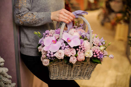 girl in gray sweater holds a basket with ribbon of purple flowers including roses , orchids and bruniaの写真素材