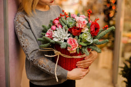 woman in gray sweater holds a bouquet with fir branches, succulents, pink roses, red poppies in red packingの写真素材