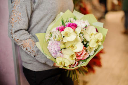 female in gray sweater holds a bouquet with beige orchids, pink roses and purple hydrangea in packingの写真素材